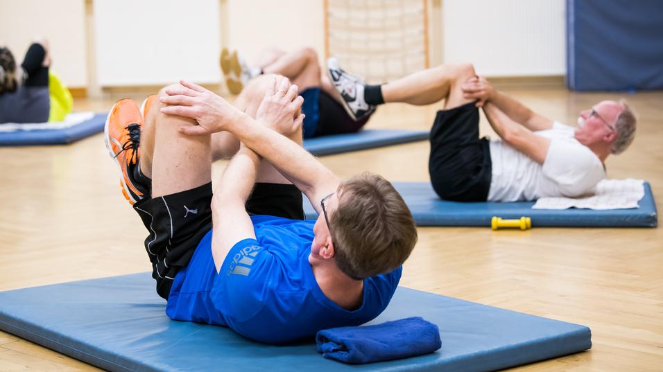 Gruppe von Personen bei Bauchmuskelübungen auf Trainingsmatten in einem Fitnessraum.